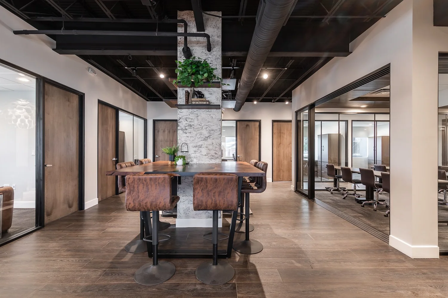Shared high-top table beside a stone-clad column, with glass-walled offices and a conference room in the background