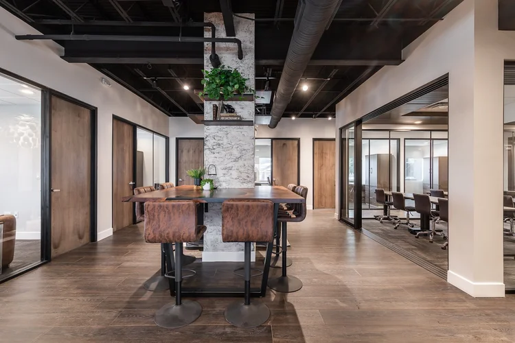 Shared high-top table beside a stone-clad column, with glass-walled offices and a conference room in the background