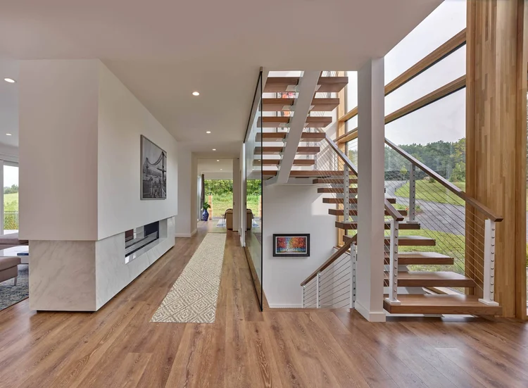 Long hallway with a wood floor leading to an open stair with wood treads, cable railings and tall wood fins along a window wall
