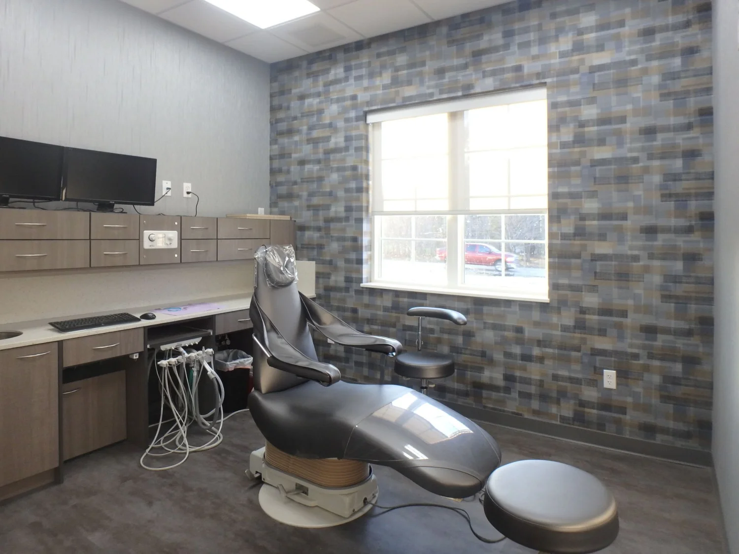 Treatment room with a dental chair, built-in cabinetry and a blue-gray tile accent wall around the window