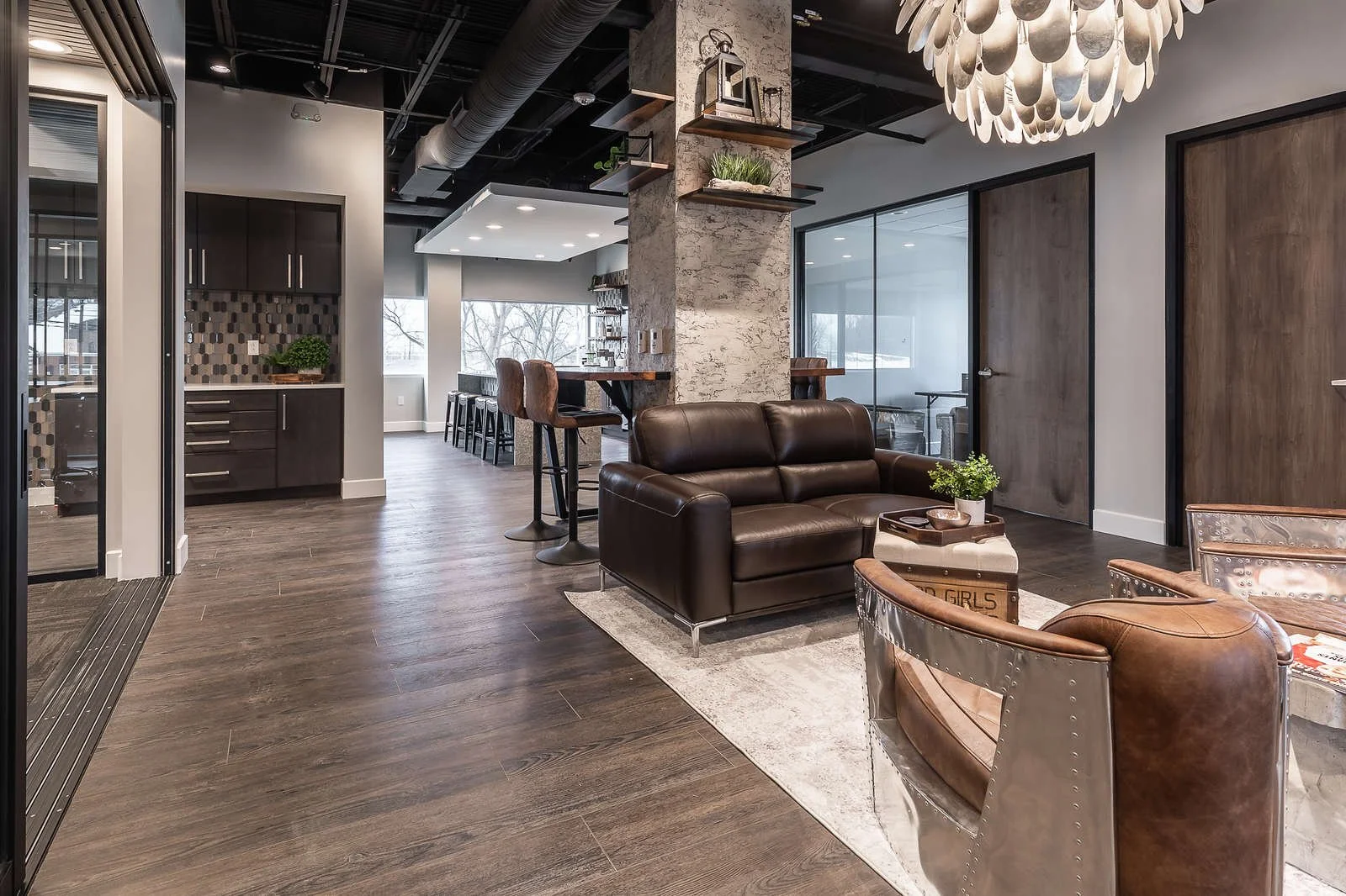 Modern office lounge area with leather sofa, armchairs, wooden coffee table, and decorative lighting fixture.