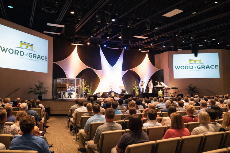 Sanctuary of Word of Grace Church during a service, with a full congregation, a stage with sculptural fabric panels and two projection screens