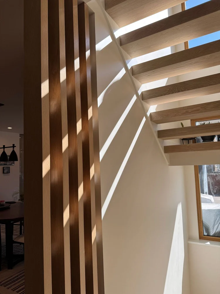 Sunlight falling in stripes through tall oak slats and across the open oak stair in the Modern Home in Cleveland