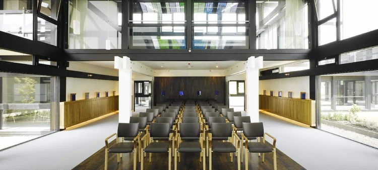 The chapel seen from the back, with wood-paneled walls, rows of chairs and daylight from above