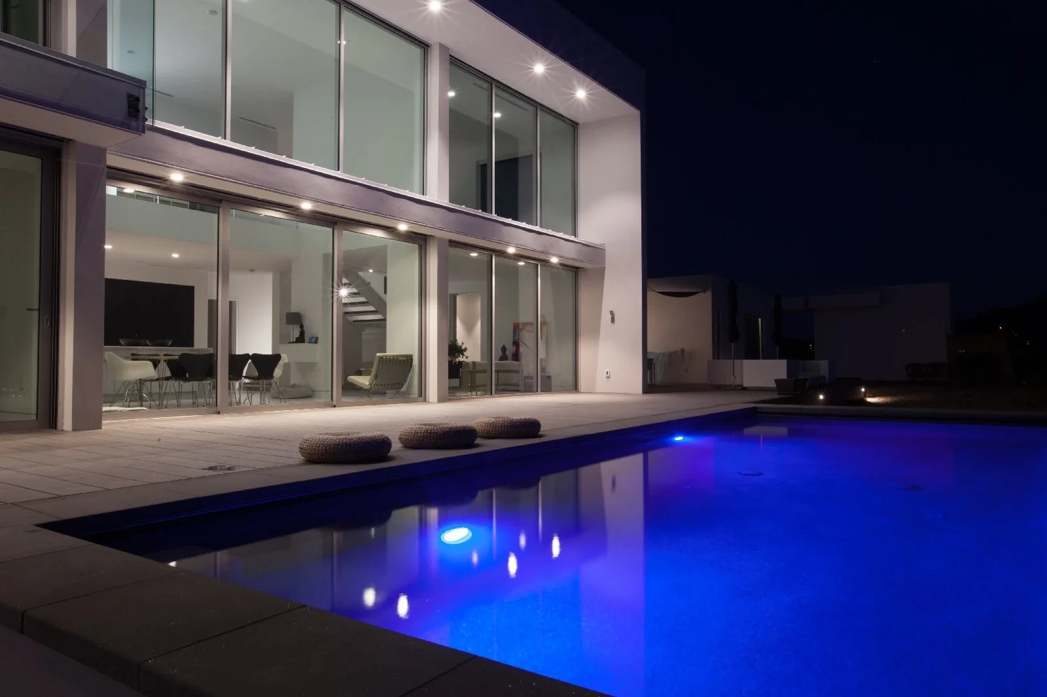 Modern glass house at dusk with a lit swimming pool in front