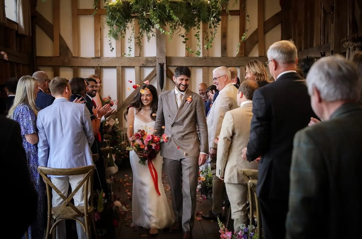 Beautiful newlyweds exit their celebrant-led wedding ceremony bu Surrey Wedding Celebrant up the aisle at gorgeous Surrey wedding venue, Gate Street Barn