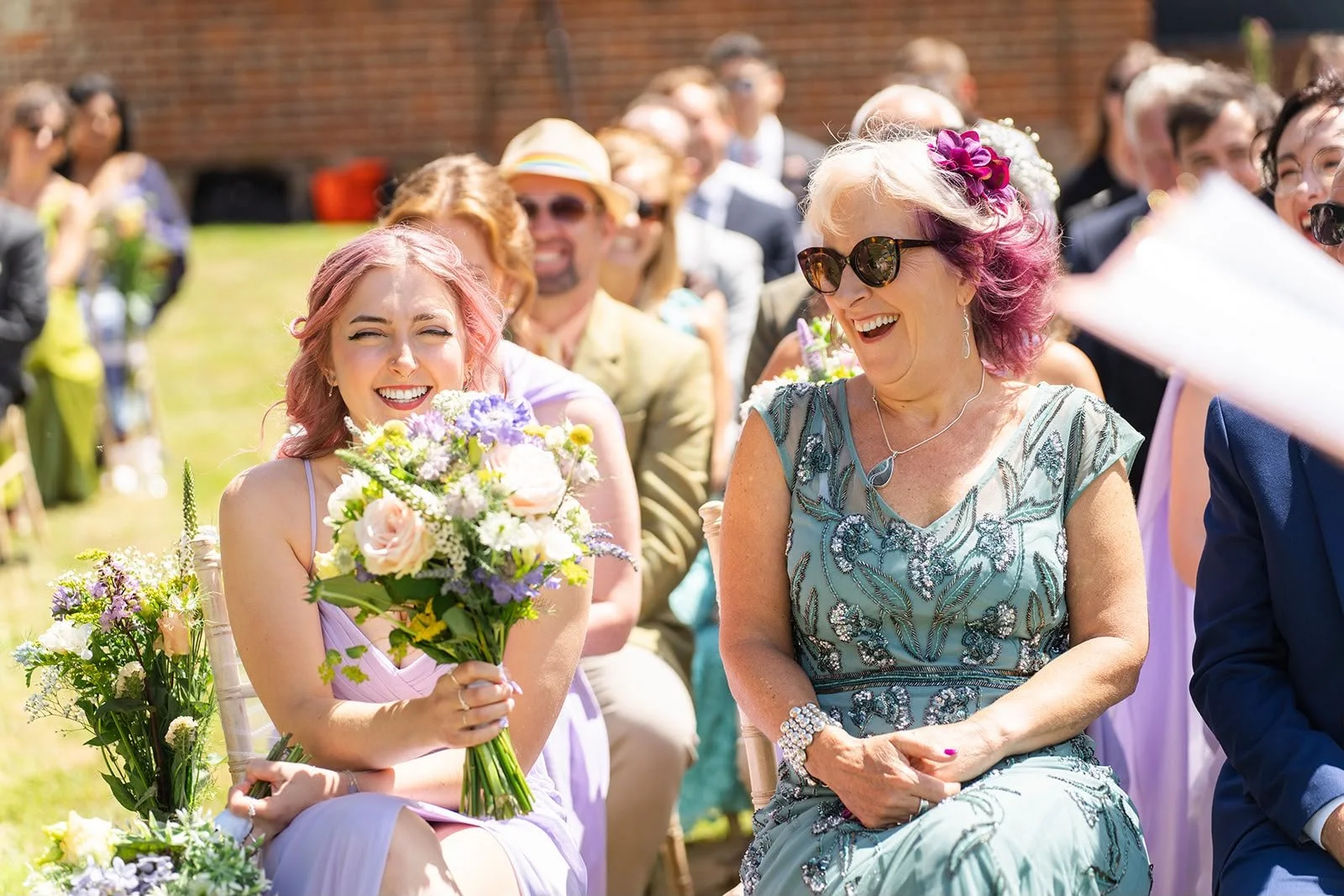 Guests laughing and smiling during a celebrant-led wedding ceremony at Sprotts Farm, Colchester, by an independent Surrey wedding celebrant. Photo: Soulful Reflection