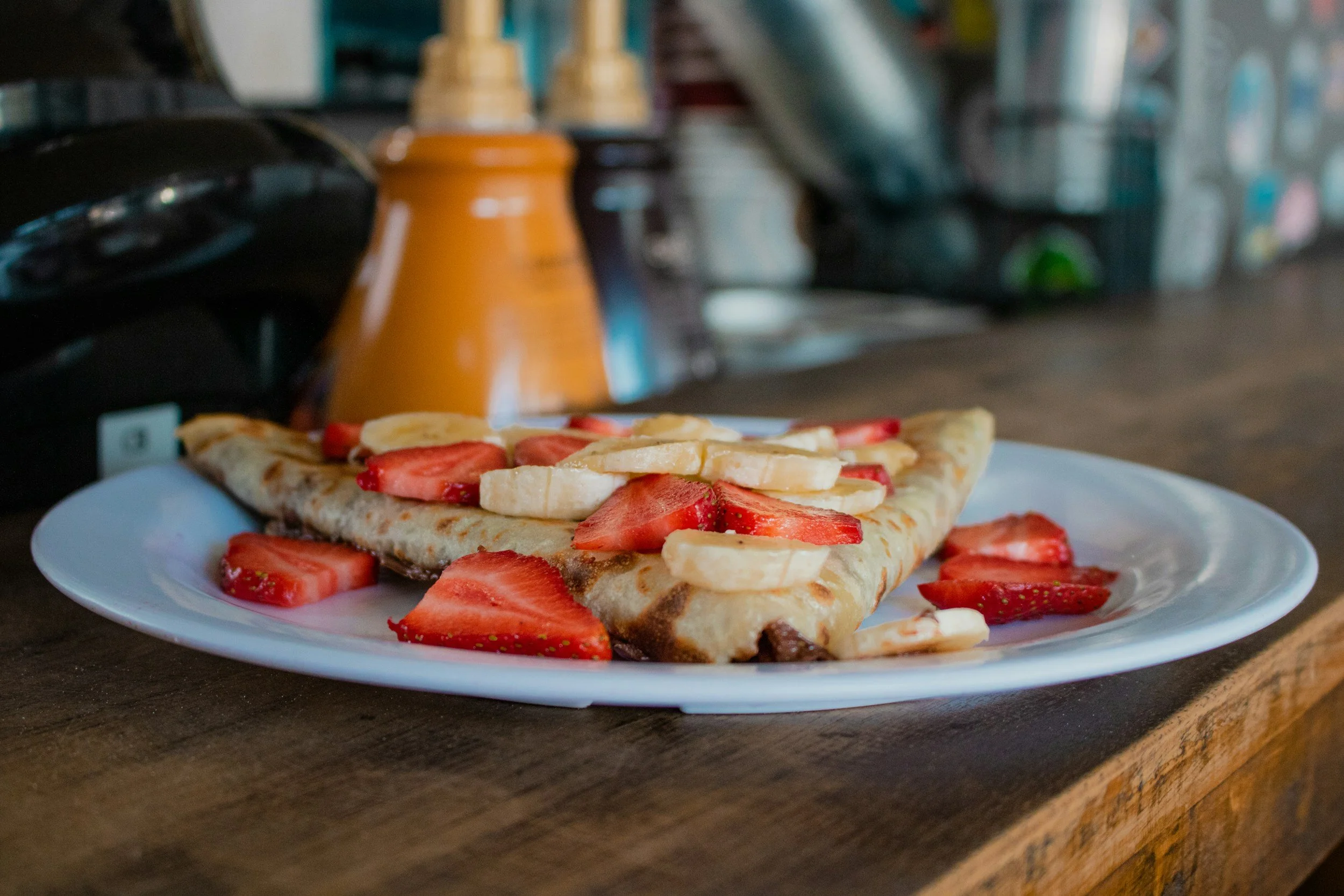 Close-up of a strawberry and banana crepe on a light blue plate.
