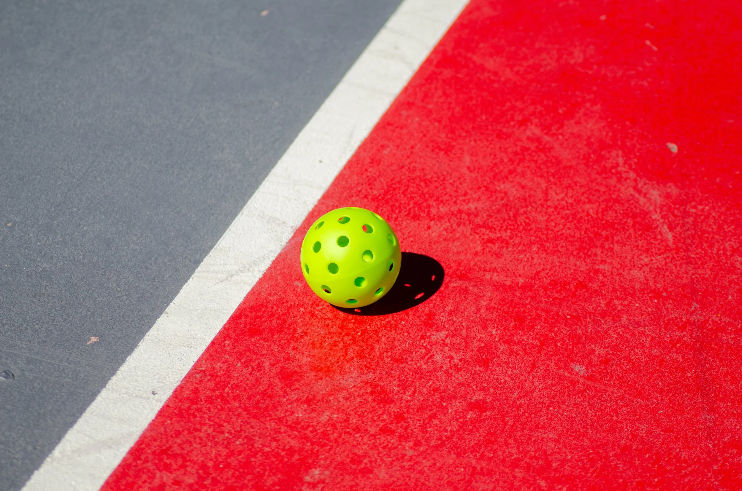 A green pickleball on a red and gray court with a white line.