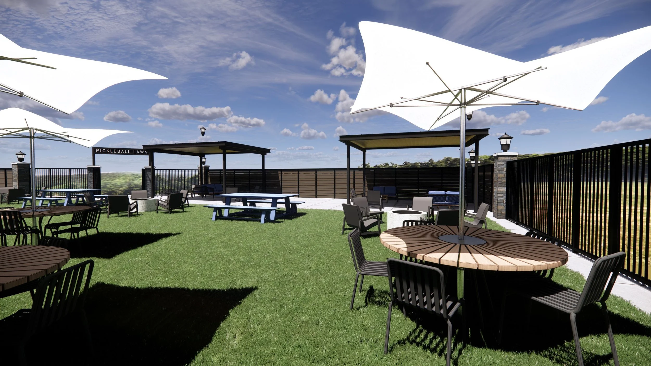 Outdoor patio with round wooden tables, black chairs, large white umbrellas, grass lawn, and black fence under blue sky with clouds.