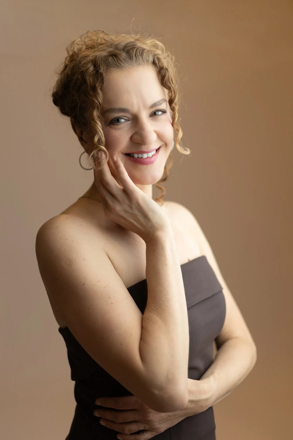 Edmonton photographer and coach Maggie Nowak smiling and wearing a dark dress against a beige background.