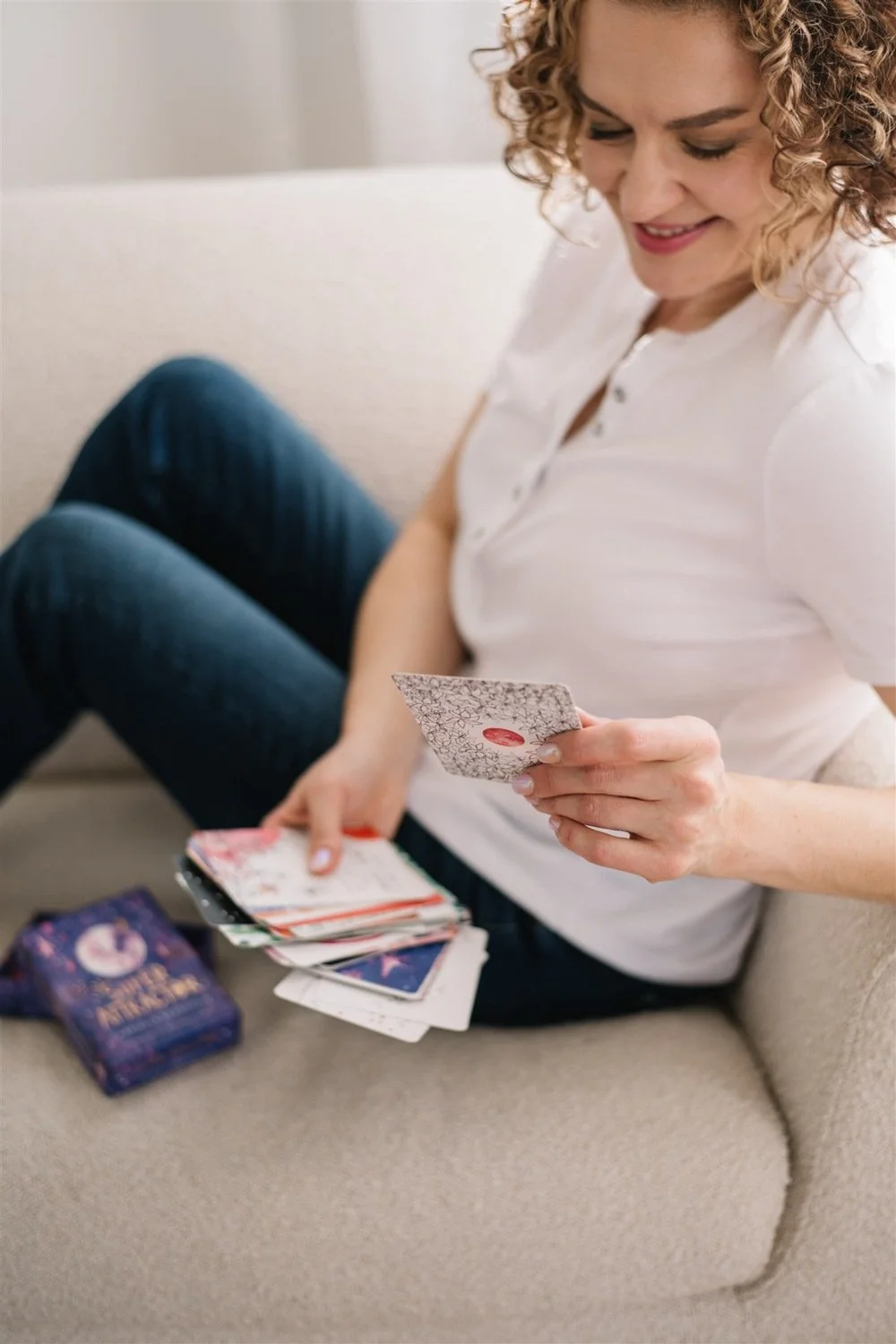 Coach and owner of Story Within, Maggie Nowak sitting on a beige couch, holding a card in her right hand.