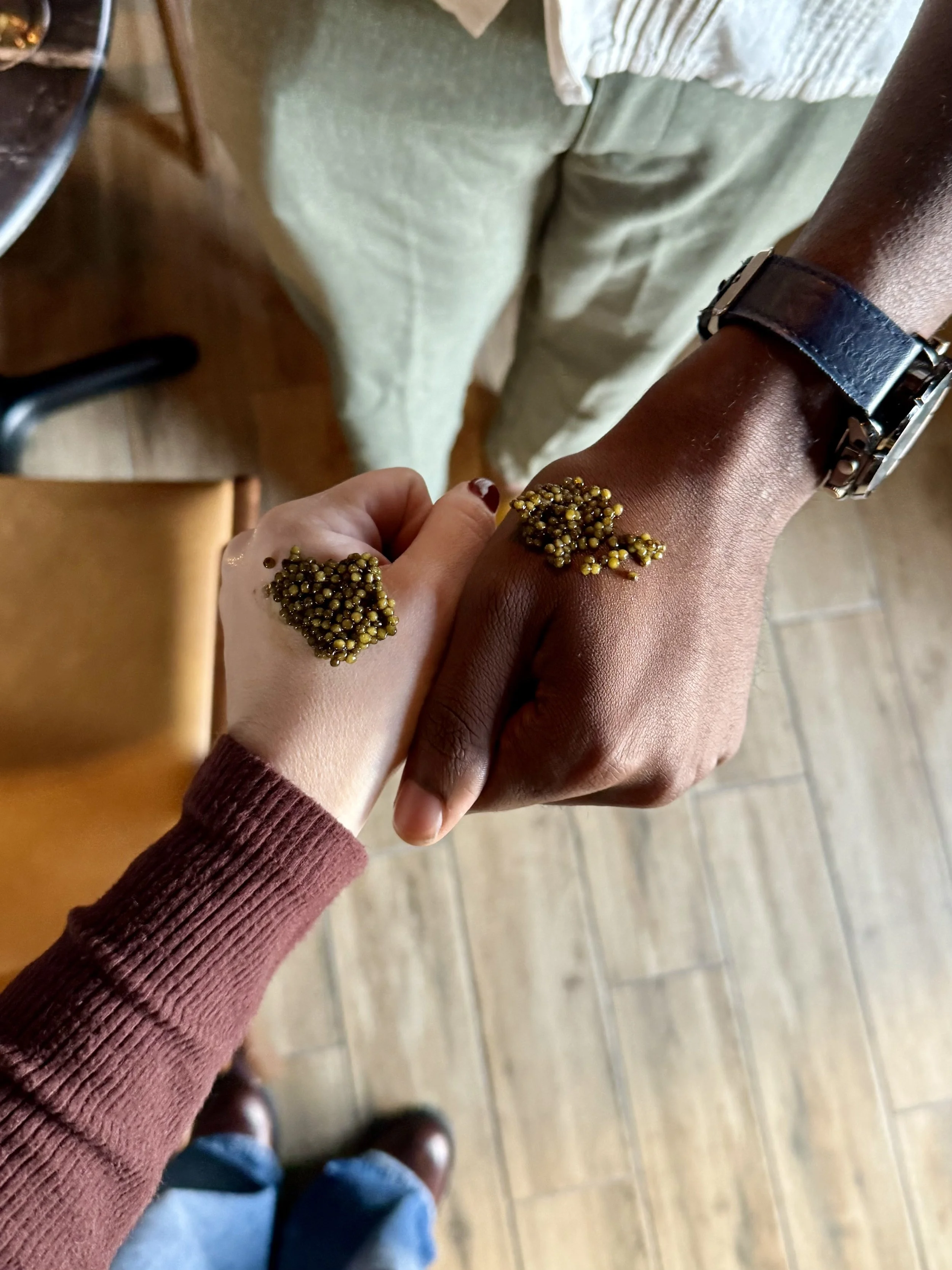 Two people's hands in fists with small servings of caviar on their hands.
