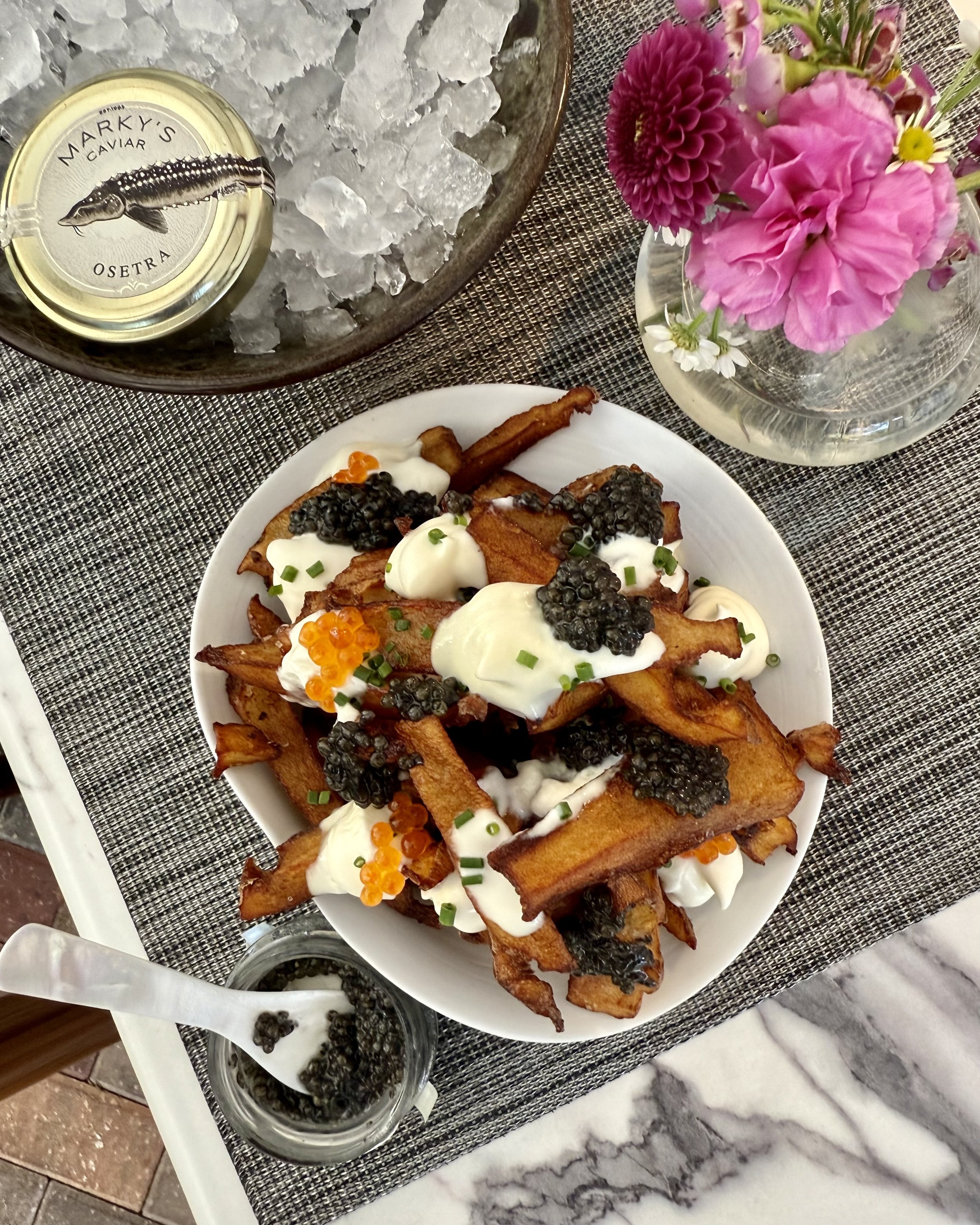 Plate of crispy French fries topped with dollops of sour cream or crème fraîche, black caviar, and green chives, with some fish roe.