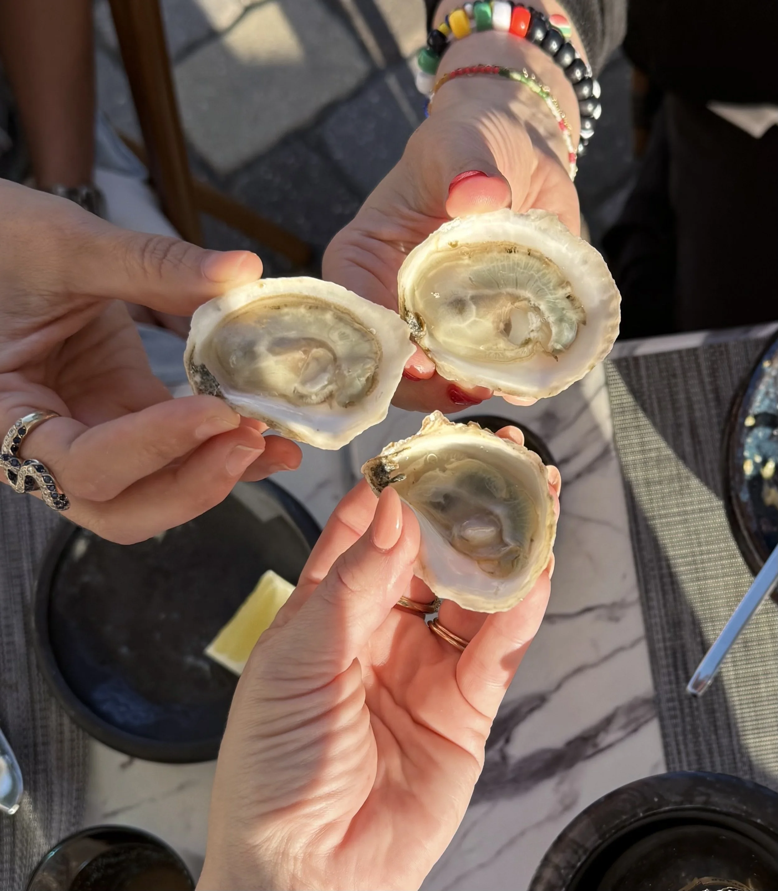 Three women's hands holding shucked oysters as if they are toasting.