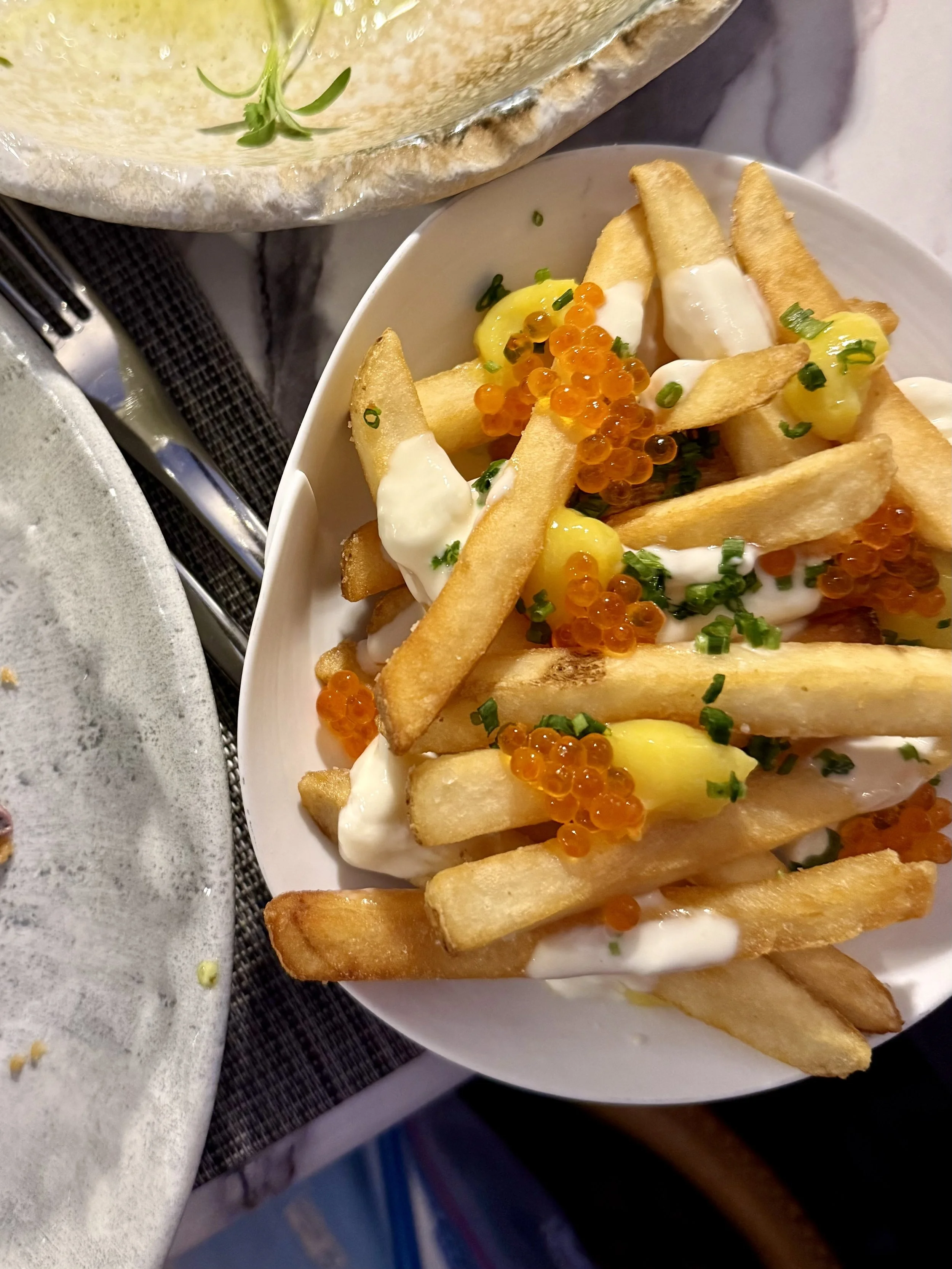 French fries topped with creamy sauce, orange fish roe, yellow dollops, and chopped chives