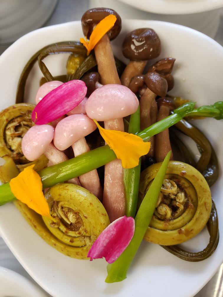 Assorted pickled vegetable, mushrooms and edible flowers on a white plate.