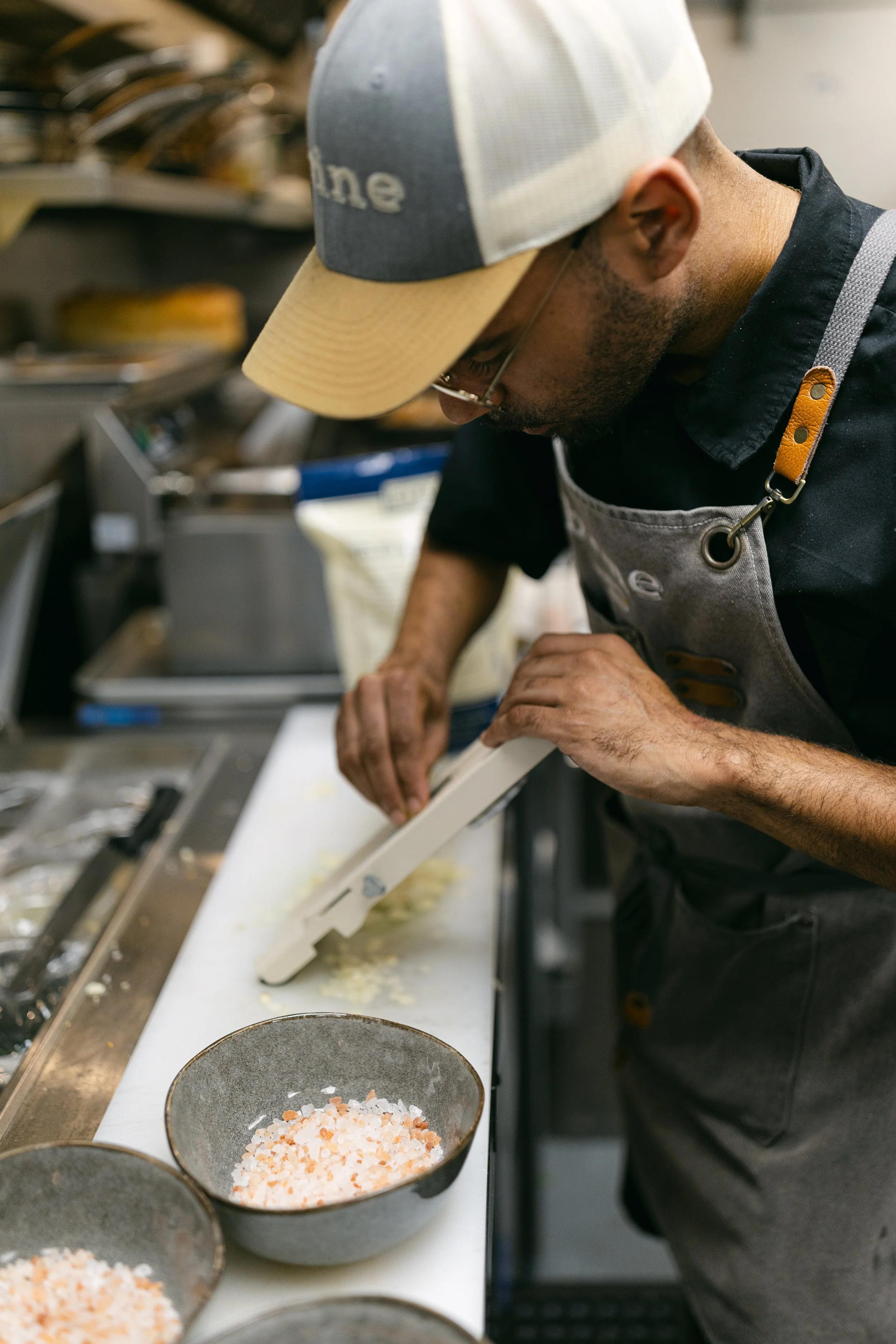 A chef in the kitchen using a mandolin to thinly slice ingredients.
