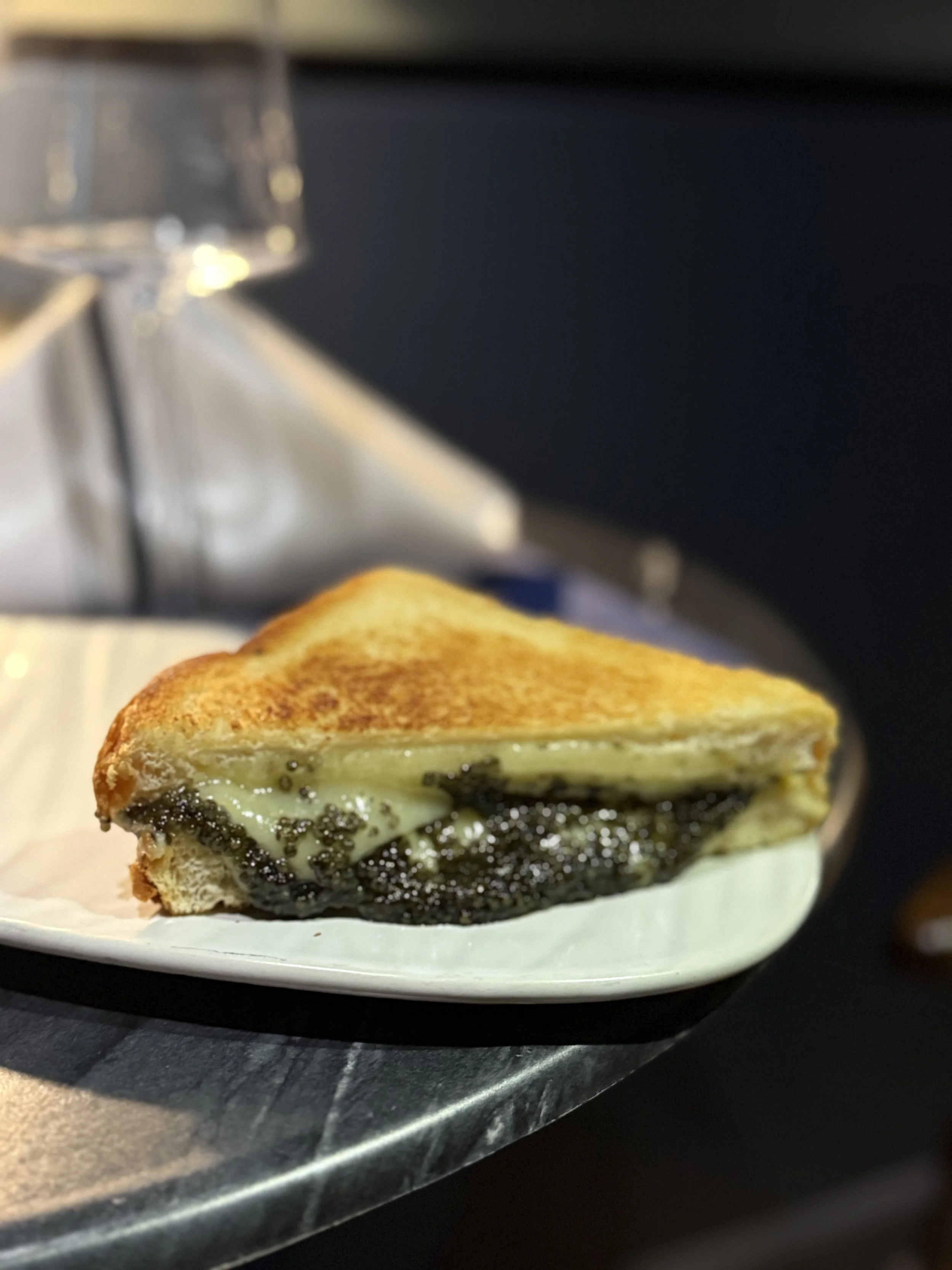 Close-up of a grilled cheese sandwich with a caviar oozing out with the cheese, served on a white plate.