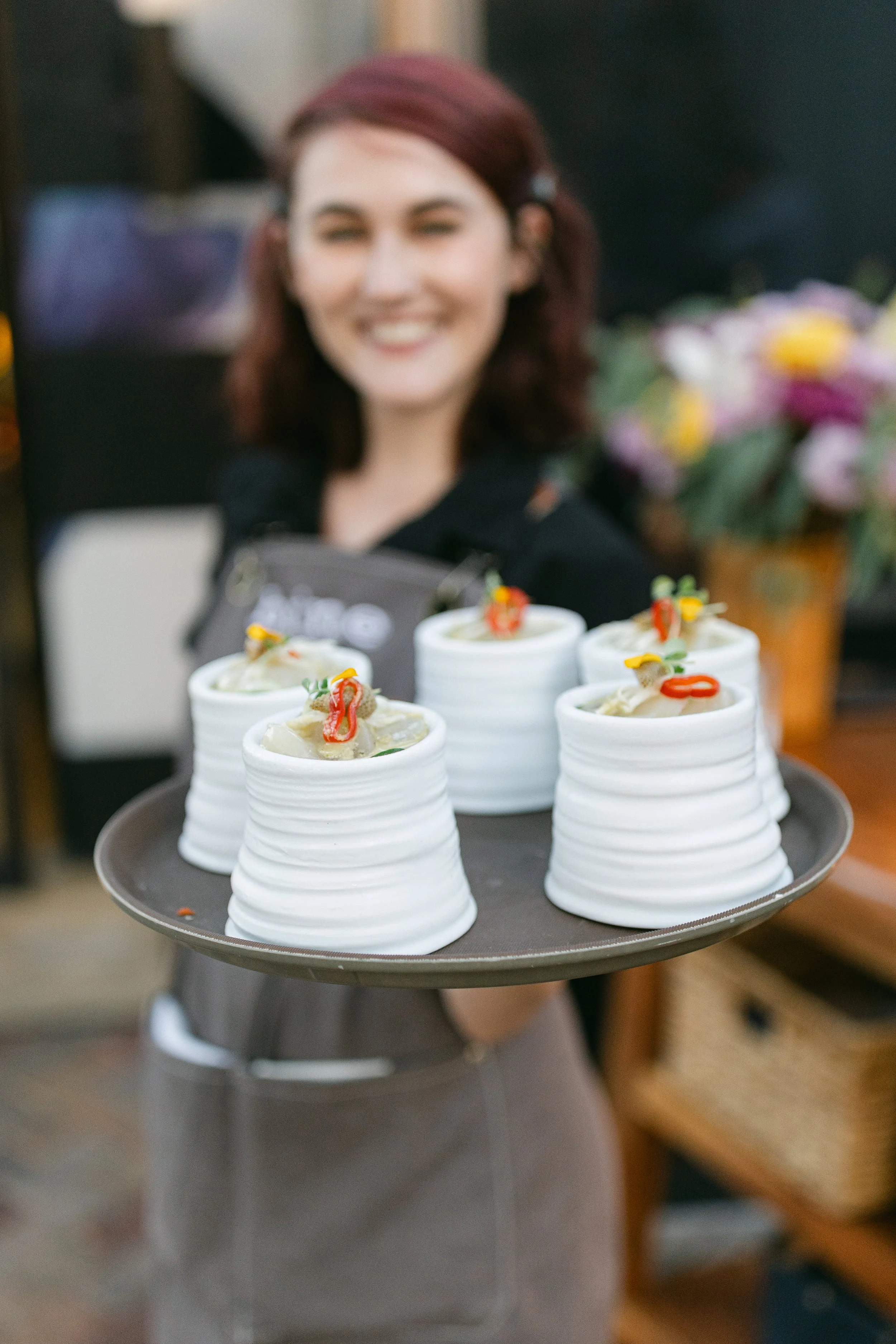 A smiling server holding up a tray full of ceramic dishes, each with a small amount of crudo and topped with orange fish roe.