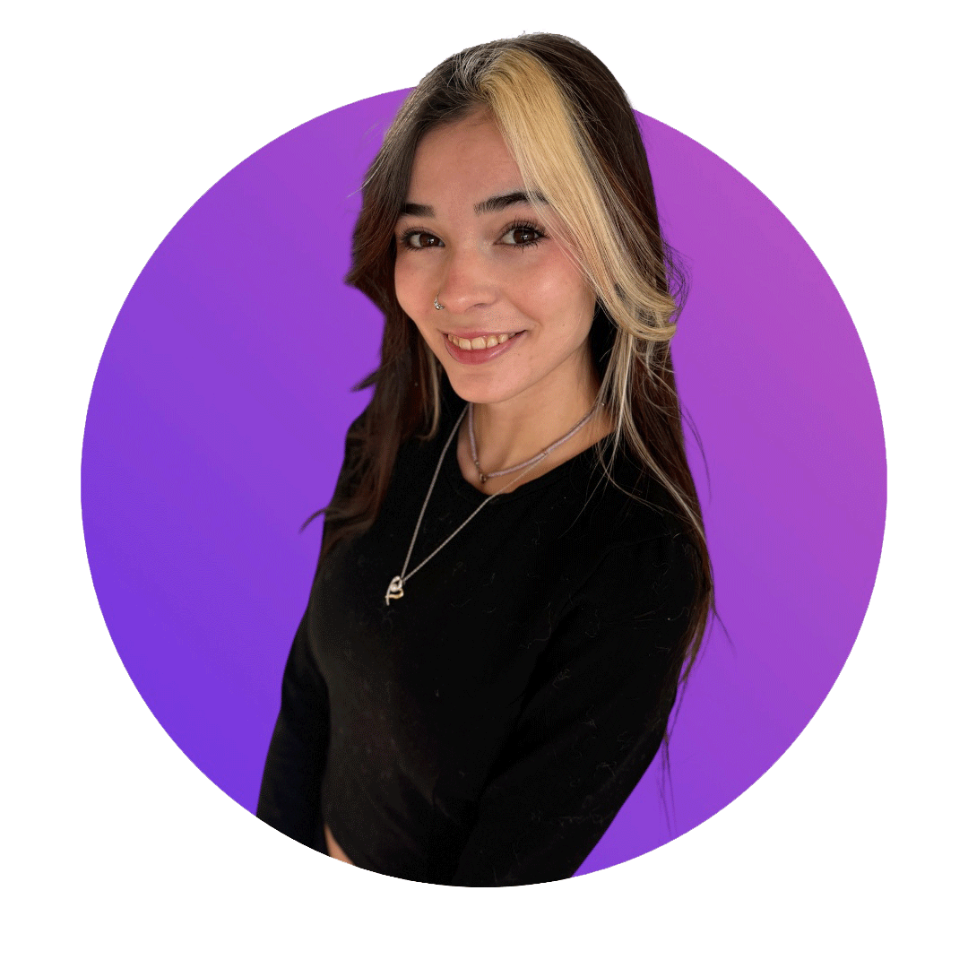 A smiling young woman with shoulder-length hair, a nose ring, and layered necklaces, posing in front of a purple background.