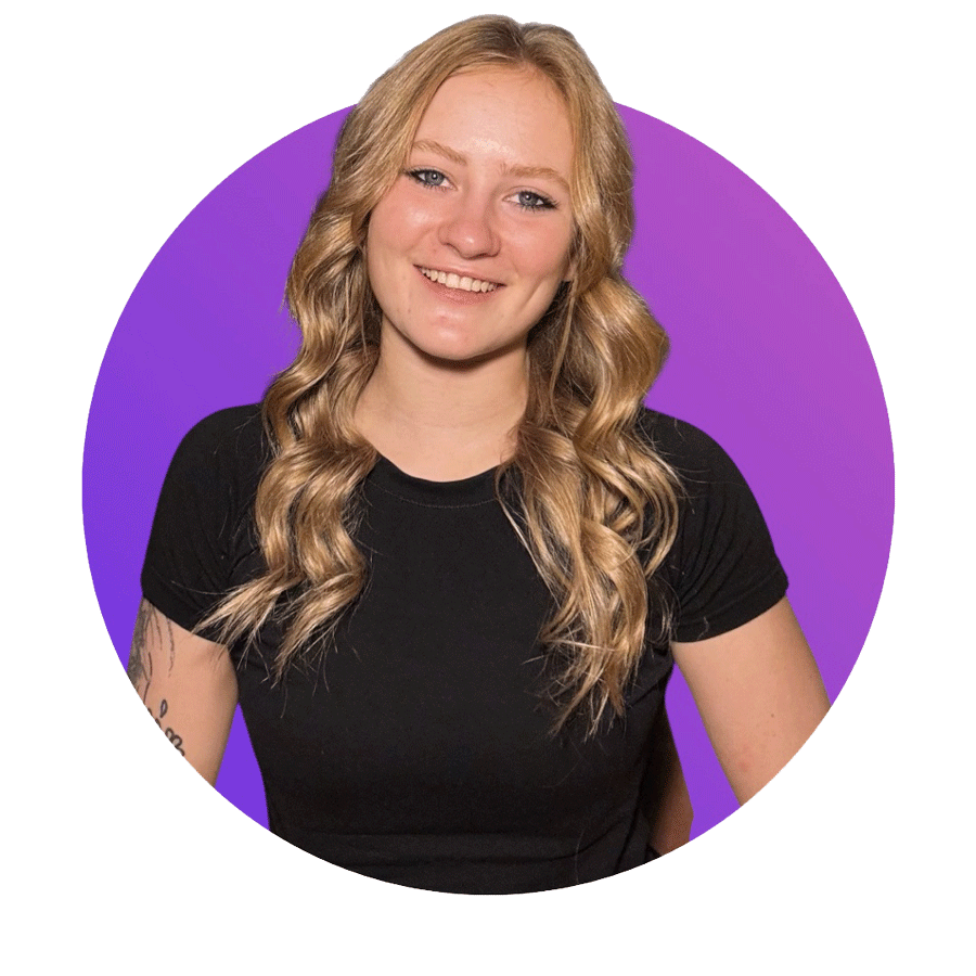 A young woman with long blonde curly hair and fair skin, smiling, wearing a black t-shirt, against a purple background.