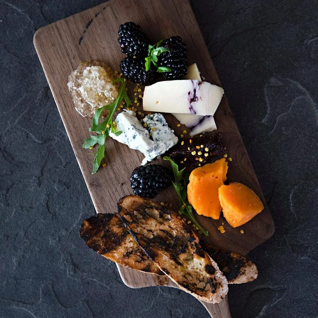 A table with various dishes including sliced bread, a salad with meat and vegetables, a drink with cucumber slices, and a plate of Asian-inspired food with sauce, garnished with microgreens and sesame seeds.