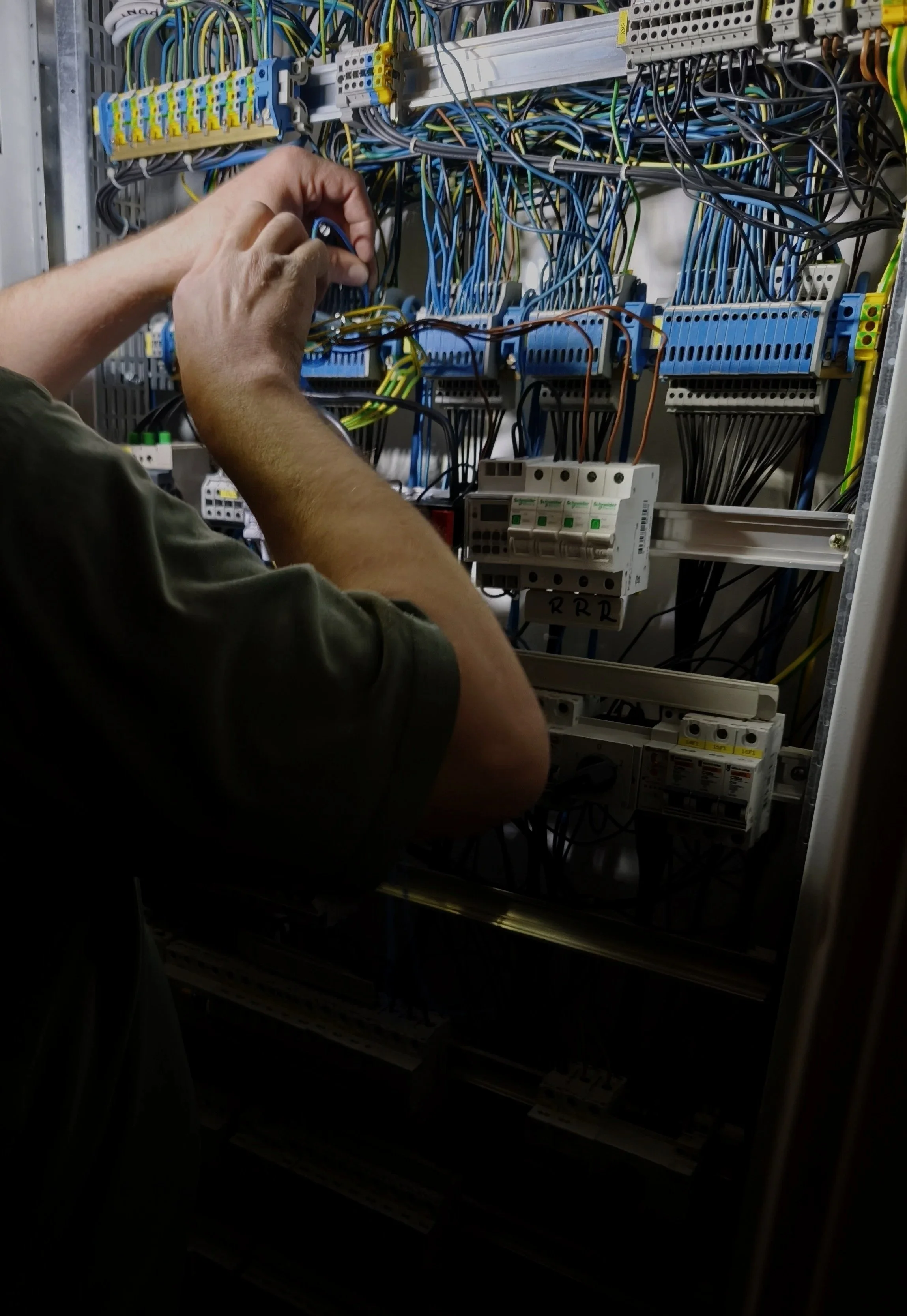 A person working on an electrical control panel with numerous wires and circuit breakers.