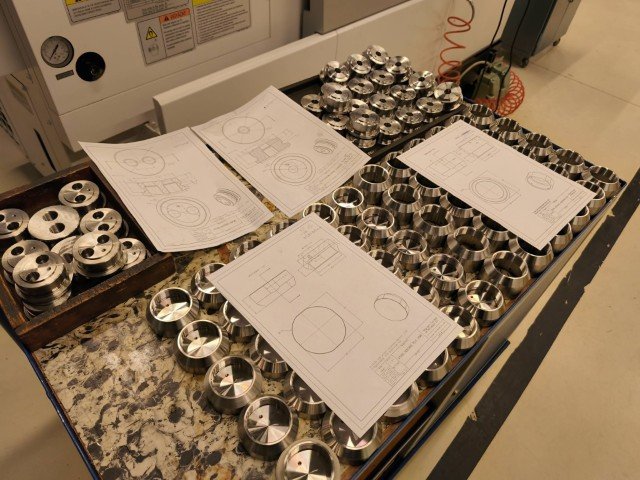 Assorted metal components and engineering blueprints on a workbench in a manufacturing or engineering environment.