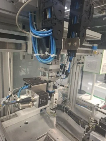 Close-up of a factory robotic arm with blue cables and mechanical components inside an industrial automation setup.