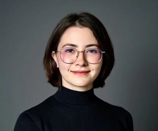 Cat Care Specialist with short dark hair and glasses wearing a black turtleneck, smiling, with a gray background.