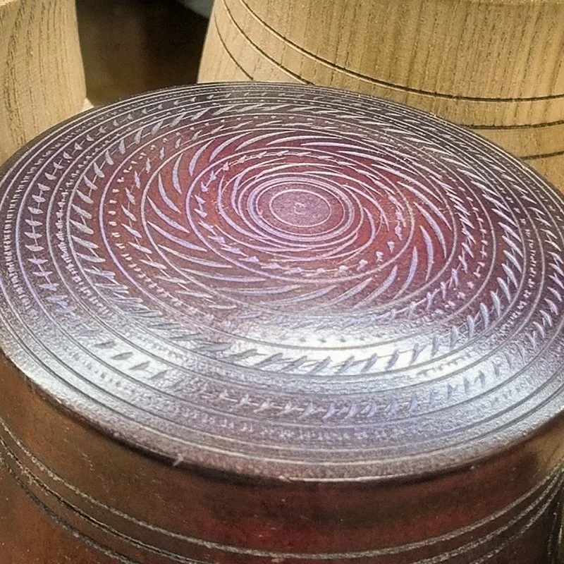A round, metallic engraving with intricate spiral patterns, placed on a wooden surface.