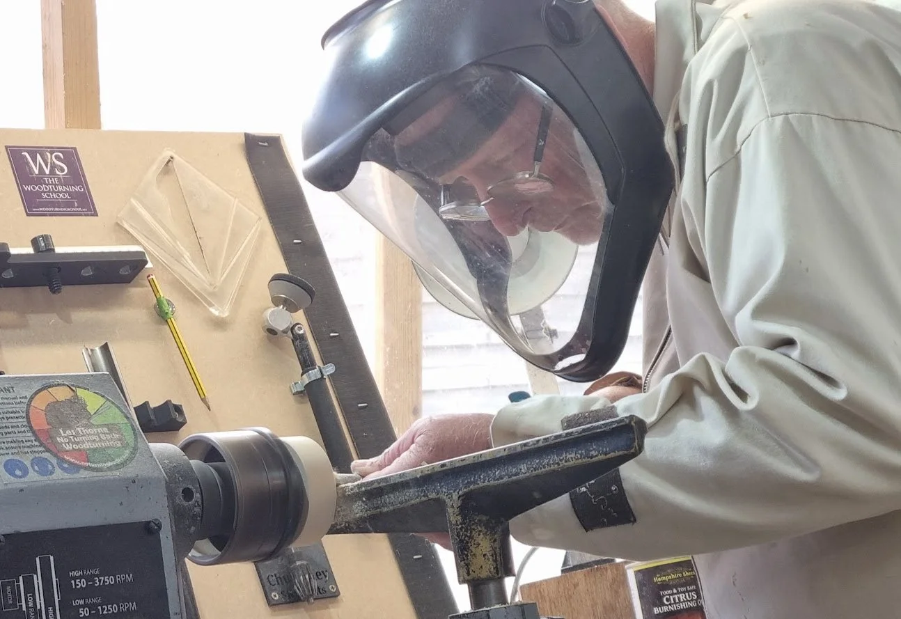Man wearing a face shield and glasses using a wood lathe in a woodworking shop.