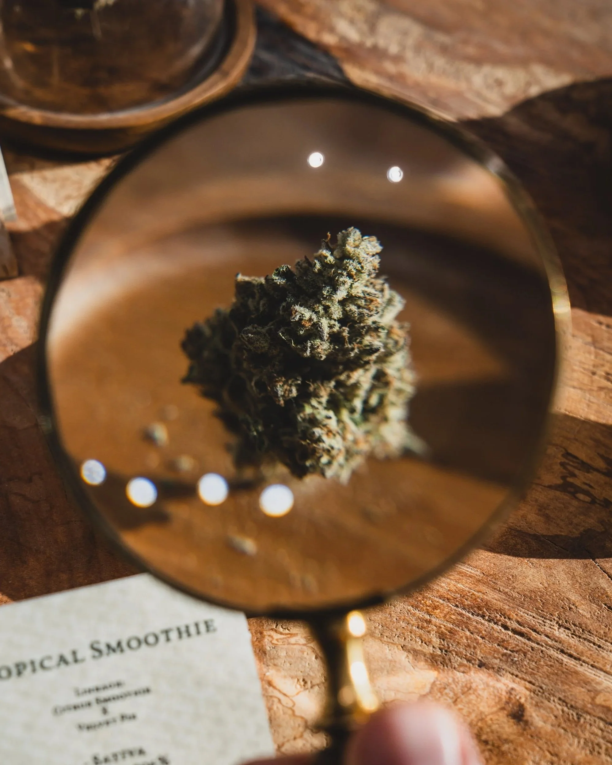 A mirror reflecting a close-up of a cannabis bud placed on a wooden surface, with a menu visible below the mirror.