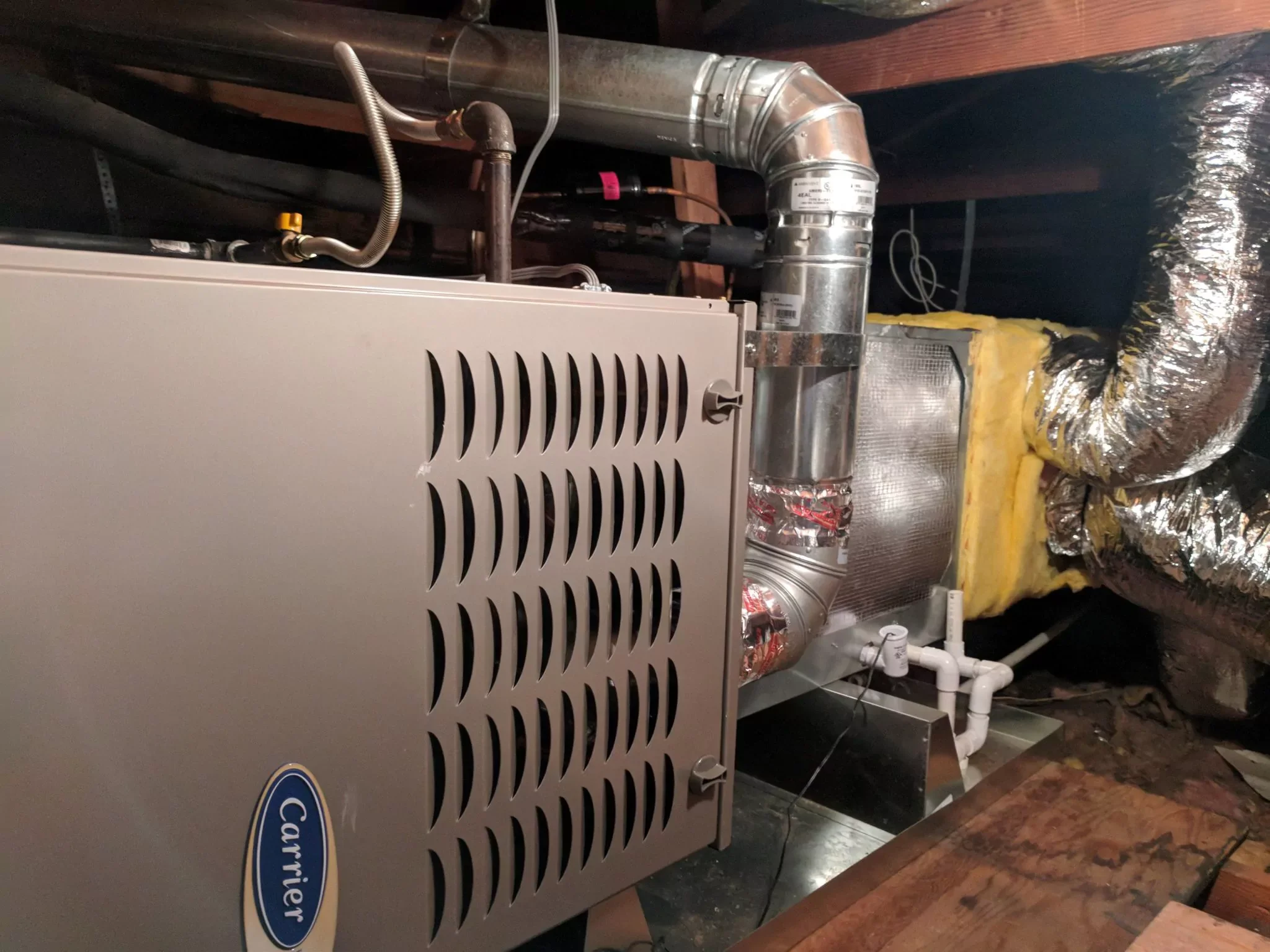An HVAC furnace system installed in an attic or crawl space with ductwork and insulation around it.