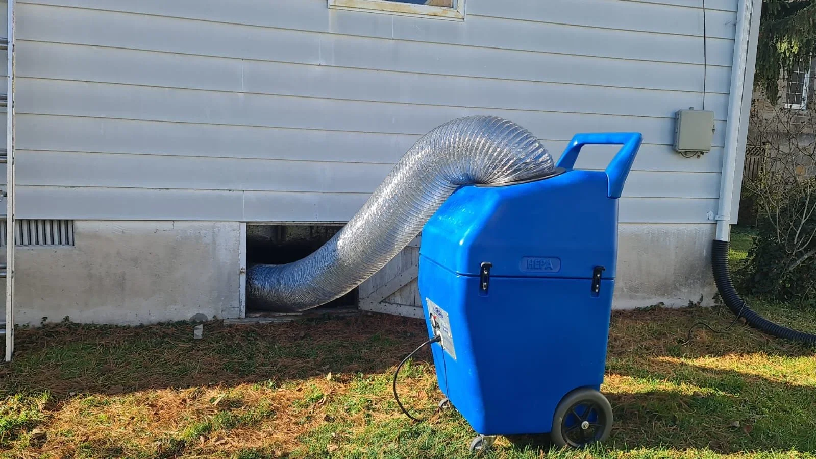 A portable air scrubber with a flexible duct connected to the house exterior, used for ventilation or drying purposes.
