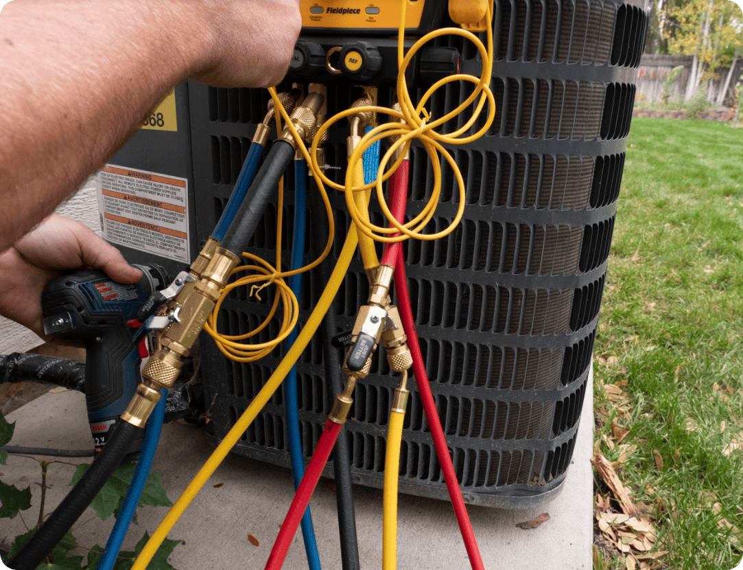 A technician using a cordless drill to connect hoses and gauges to an HVAC unit for maintenance or repair.