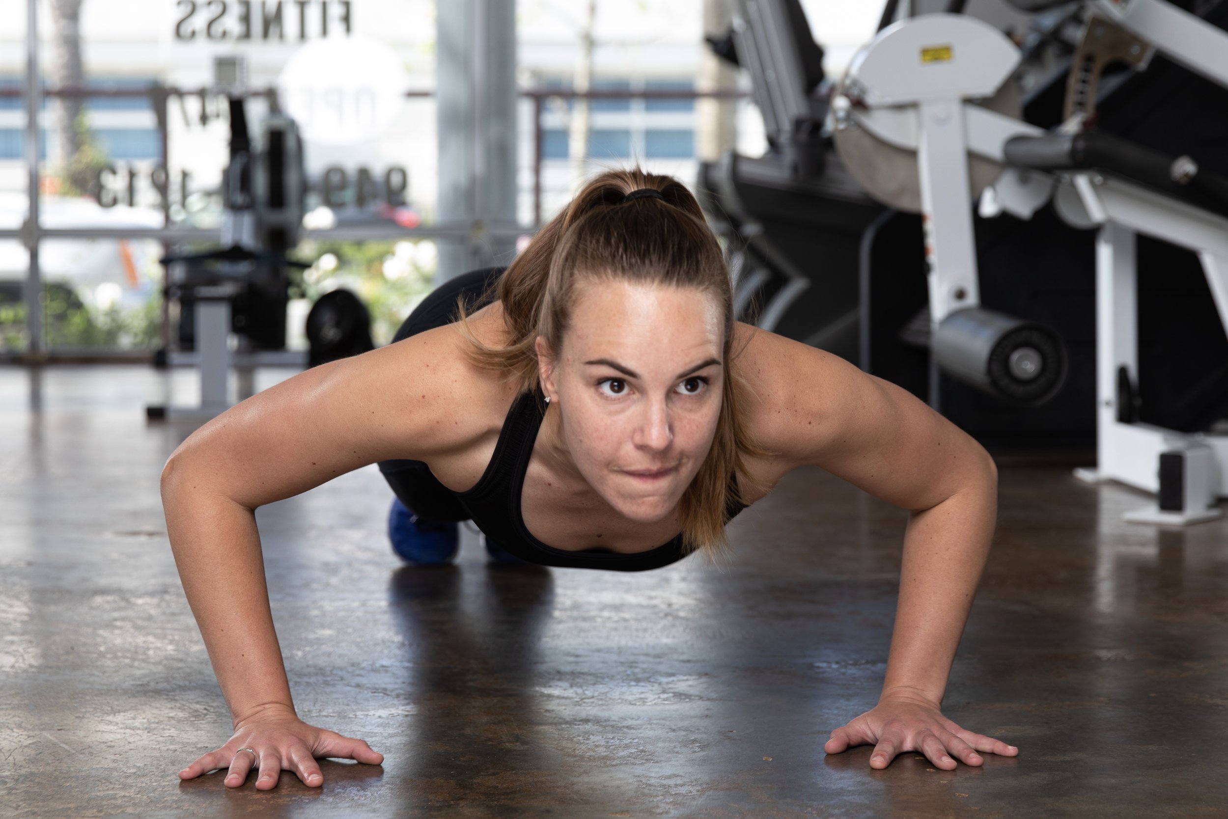 Woman in workout clothes doing push-up on gym floor.