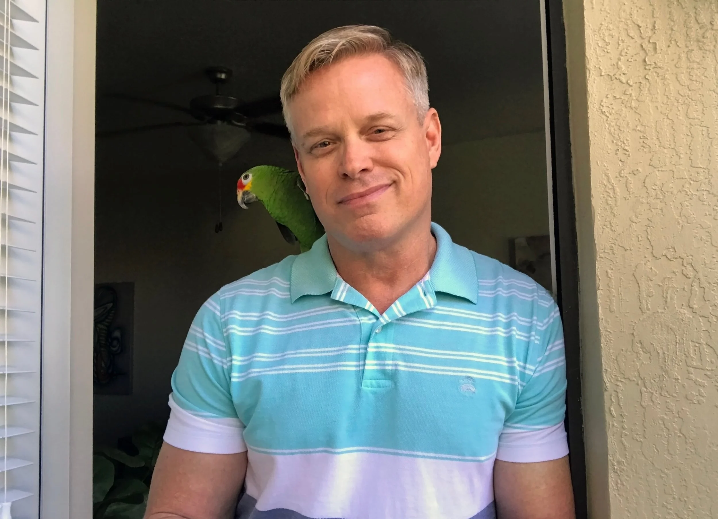 RJ Starr standing in a doorway with his parrot Pepper on his shoulder.