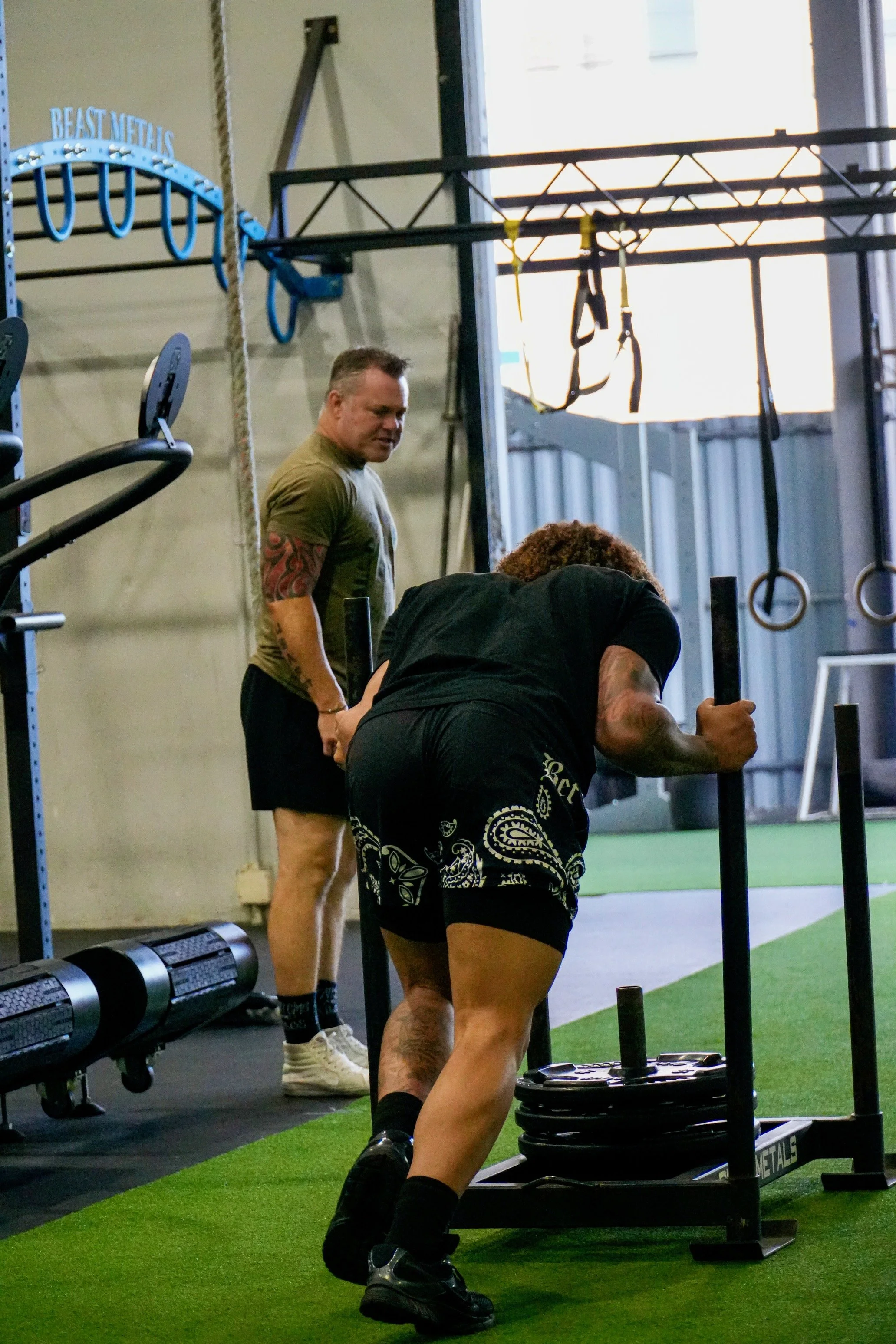 Two people exercising with battle ropes and on artificial turf in a gym.