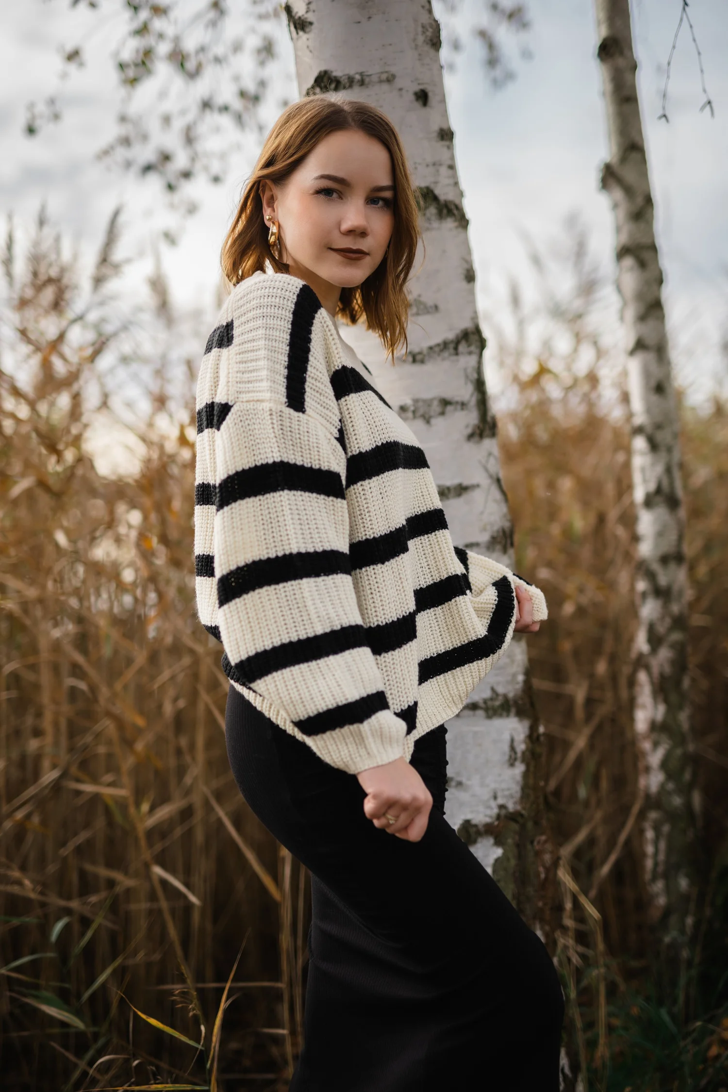 Portrait einer Frau im gestreiften Pullover vor hellen Birken und herbstlich braunen Gräsern