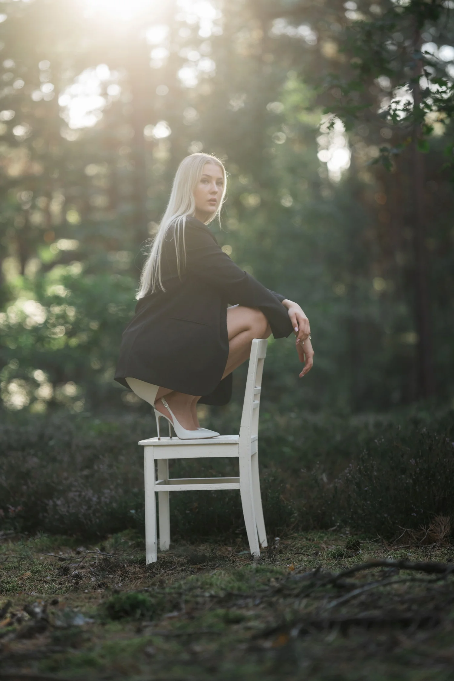 Sitzportrait auf weißem Stuhl im Wald mit hellem Streulicht von links oben