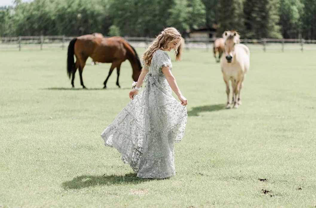 Woman in floral dress walking in a field with two horses