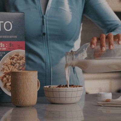 Person pouring milk into a bowl of cereal on a kitchen counter.