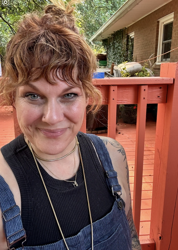 selfie of a woman with red hair smiling on an outdoor porch