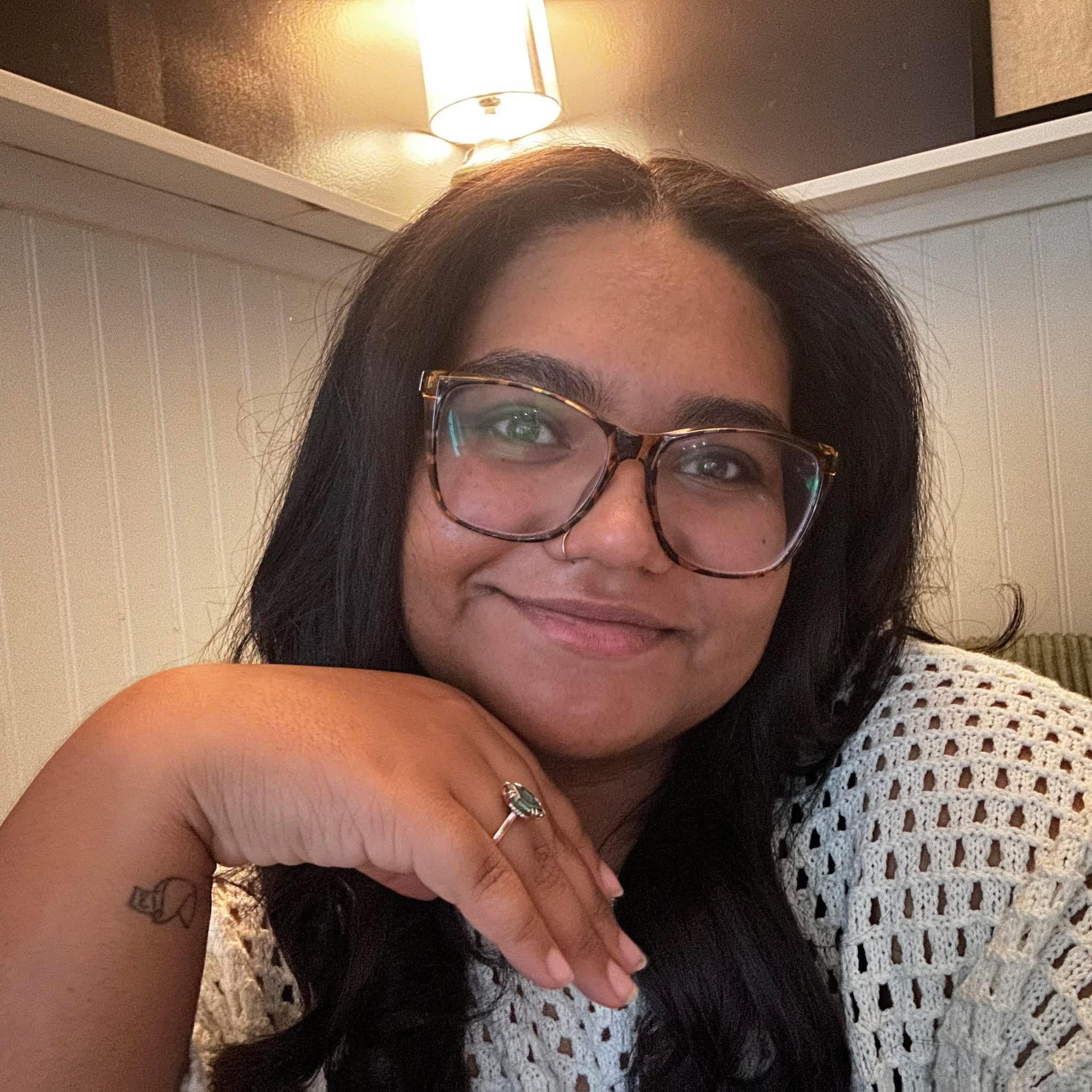 Selfie of a young woman with large round glasses smiling in an indoor setting