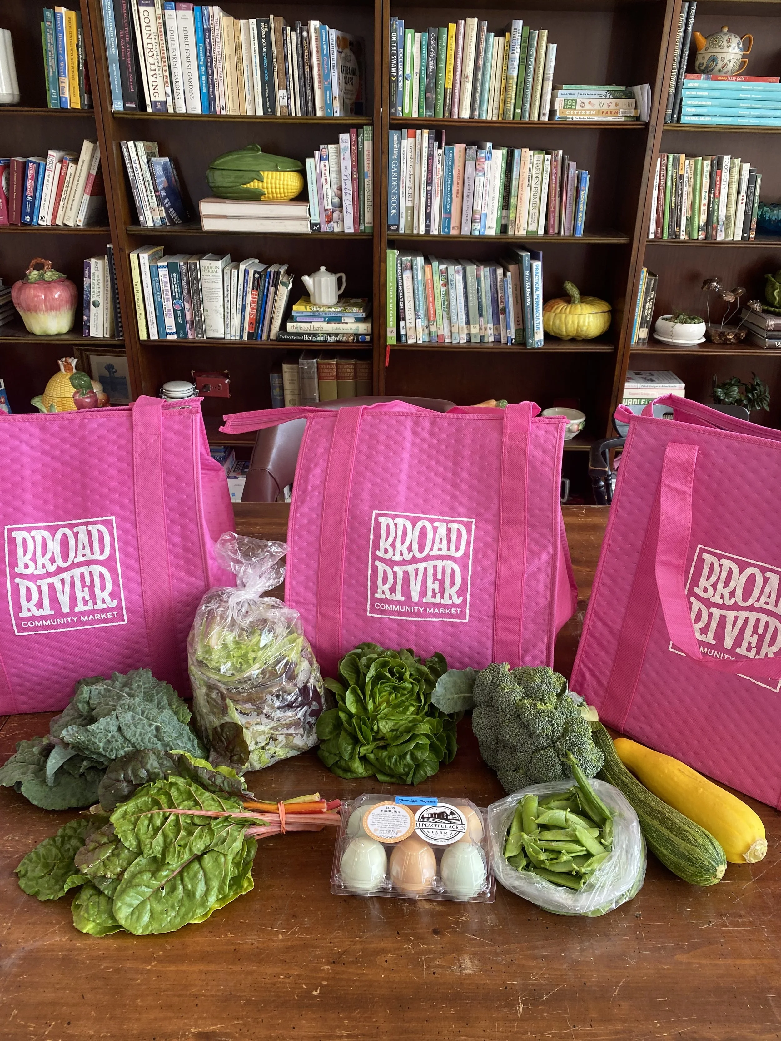 Pink bags with Broad River Market written on them and various produce items sitting on a table