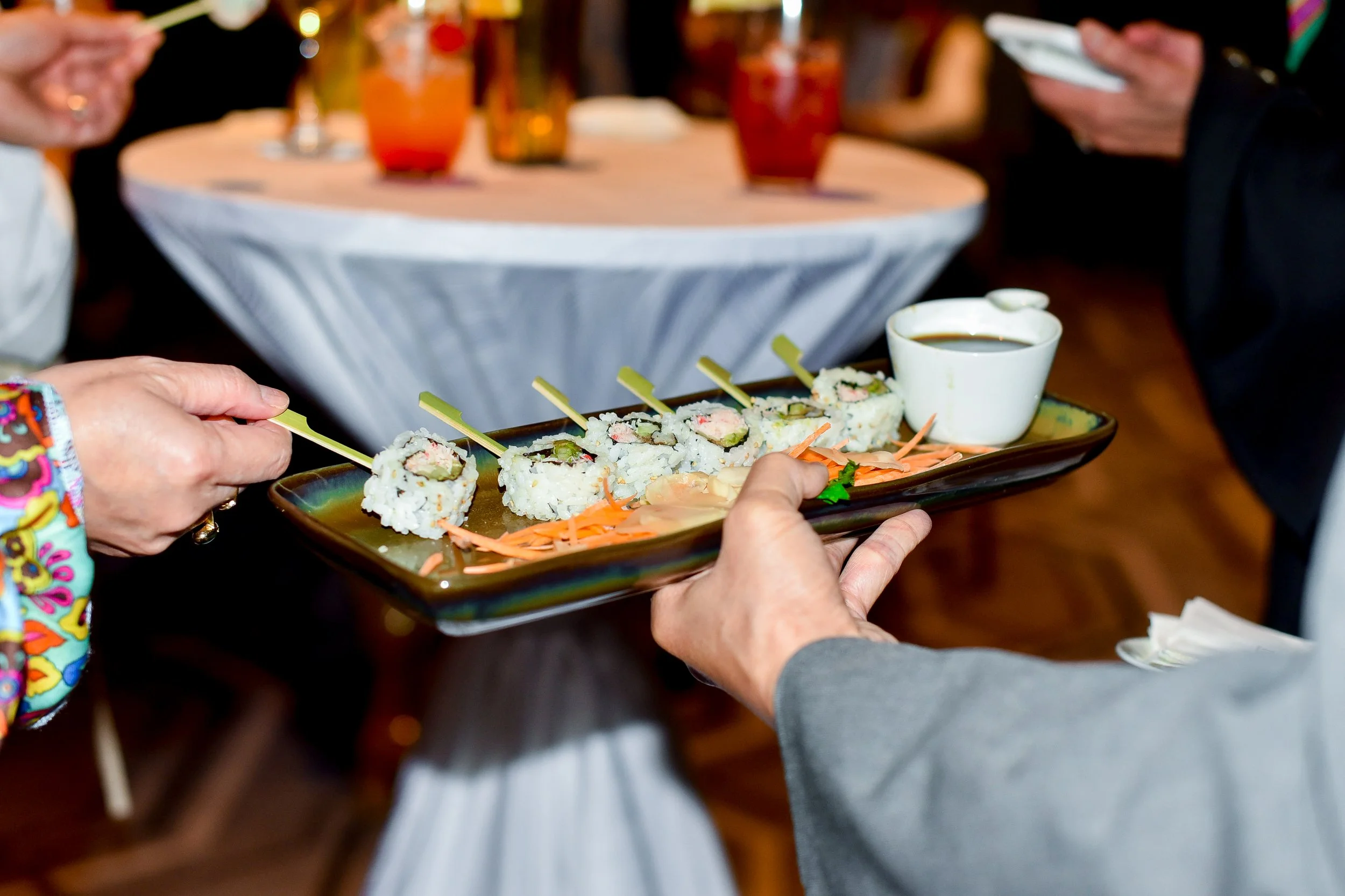 A person serving sushi rolls on a black rectangular plate at a social gathering.