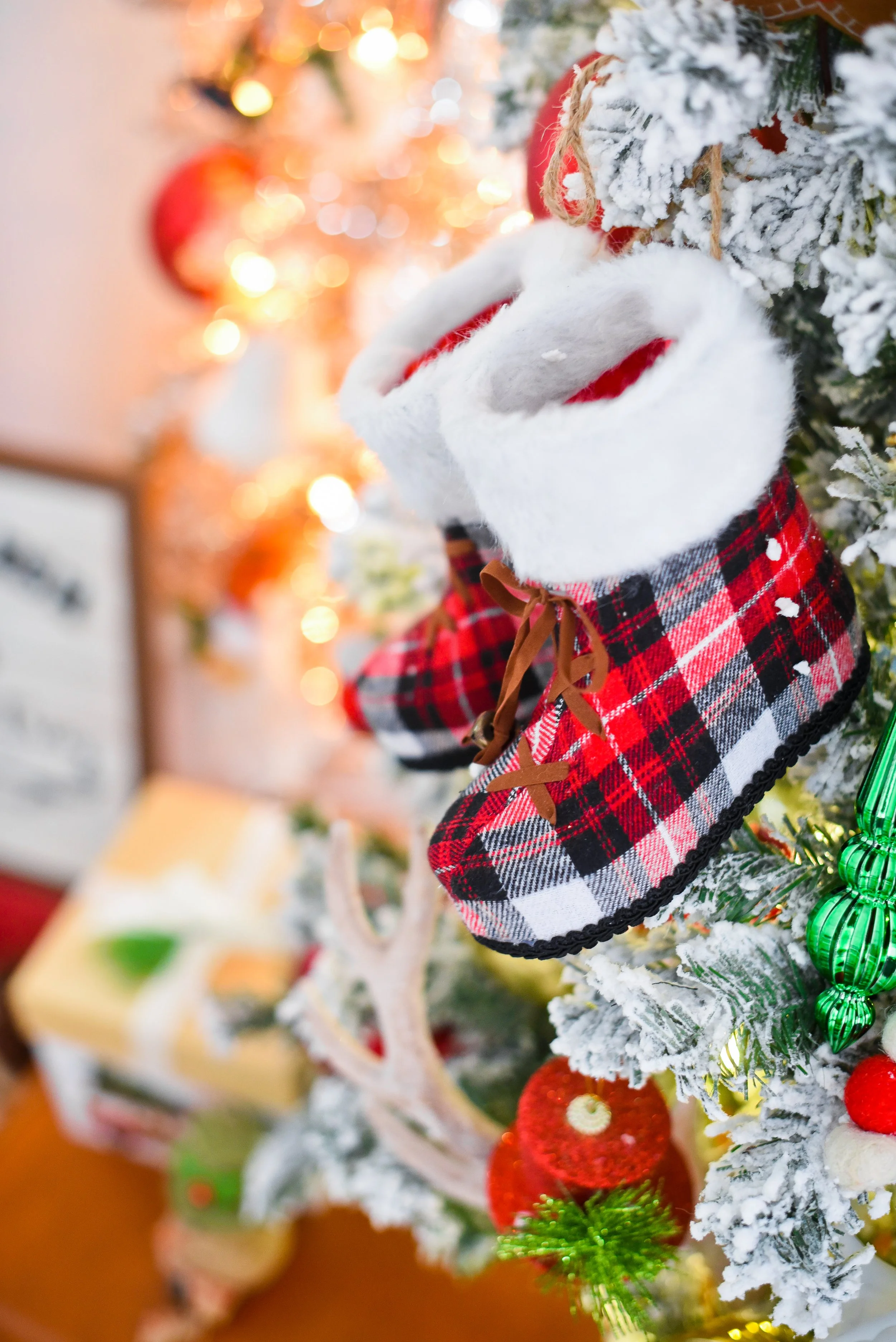 Close-up of Christmas stockings with plaid patterns hanging on a decorated Christmas tree with snow-like flocking, ornaments, and lights.