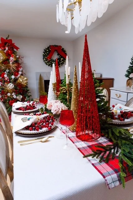 Christmas table decorated with red and gold tree decorations, candles, cranberries, and greenery, with a Christmas tree and wreath in the background.